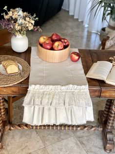 a wooden table topped with apples next to a basket of bread and fruit on top of it