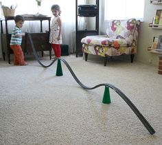 two young children playing with toy cars on the carpet in their living room, while one child watches