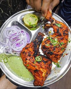 a person is cutting up some food on a silver platter with onions and cucumbers