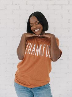 A simple crewneck tee that reads, "THANKFUL" in skinny letters. Model is shown in size medium. Model info: 5’4, normally a size medium in tops and dresses, and size 28 or 29 in pants. D&E Tees. Thankful Grateful Shirts, Orange Cotton Graphic Tee, Simple Crewneck, Casual Thanksgiving Graphic Print T-shirt, Mustard Graphic Print Cotton T-shirt, Thanksgiving Graphic Print Crew Neck T-shirt, Thanksgiving Cotton Graphic Print T-shirt, And Dresses, Size Medium