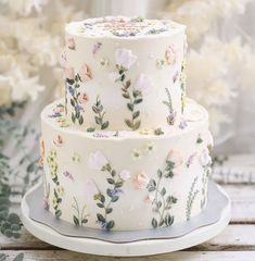 a three tiered cake decorated with flowers and greenery sits on a white plate