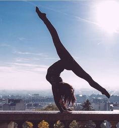 a woman doing a handstand on top of a building with the sun in the background