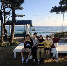 a group of people sitting on top of a white bench near the ocean and trees