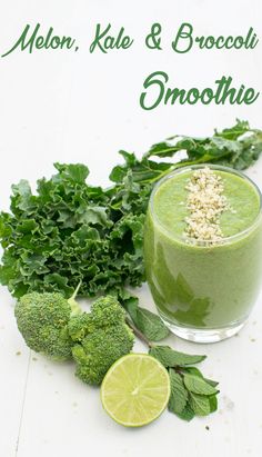 a green smoothie in a glass surrounded by greens and limes on a white surface