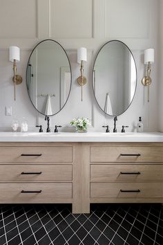 two round mirrors are above the double sinks in this bathroom with black tile flooring