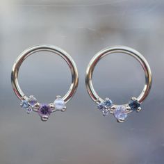 two piercings with different colored stones are shown in front of a glass window,