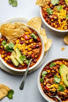 three bowls filled with chili, corn and avocado next to tortilla chips