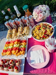 a table topped with lots of food on top of a pink cloth covered picnic table