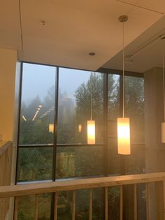 some lights hanging from the ceiling in a room with large windows and trees behind them