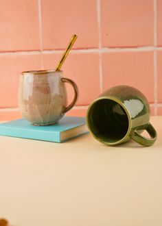 a coffee mug sitting on top of a book next to a cup with a straw in it