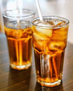 two glasses filled with ice tea sitting on top of a wooden table