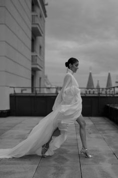 a woman in a white dress is walking down the sidewalk with her long flowing skirt