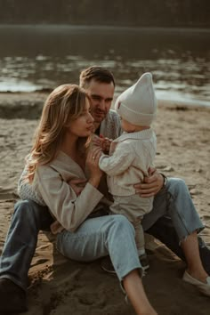 a man and woman sitting on the beach with their baby in his lap, holding onto each other