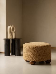 a round ottoman sitting on top of a white floor next to a vase and table