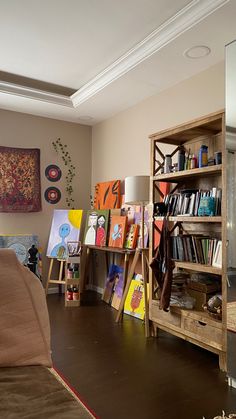 a living room filled with lots of books and art on the wall next to a couch