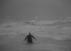 a person standing in the ocean with their arms spread out to catch some waves on a gloomy day