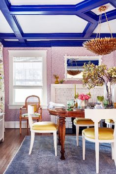 a living room filled with furniture and a blue painted ceiling above a dining table surrounded by yellow chairs