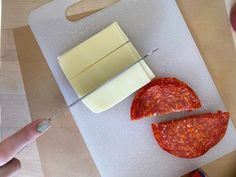 a person cutting cheese with a knife on a cutting board next to other food items