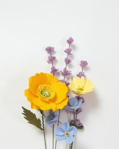 three different colored flowers in a vase on a white surface with purple and yellow flowers