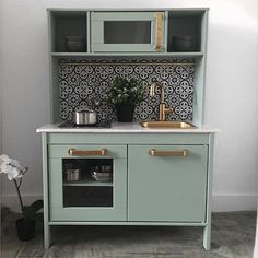 a small kitchen with green cabinets and white counter tops, gold pulls on the handles