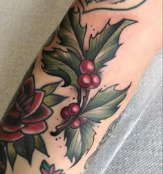 a close up of a person's leg with tattoos on it and holly leaves