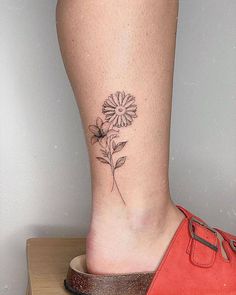 a woman's foot with a flower tattoo on the side of her leg and an orange shoe