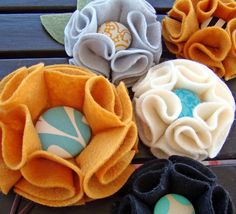 four fabric flower brooches sitting on top of a wooden table next to each other