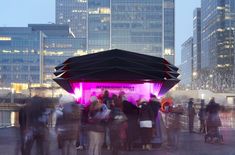 a group of people standing around in front of a building with pink lights on it