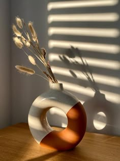 a vase with some dried flowers in it on a table next to a shadow cast wall