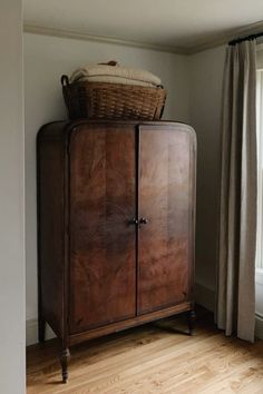 a wooden cabinet sitting in the corner of a room with a basket on top of it