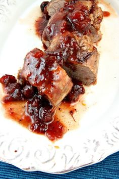 a white plate topped with meat covered in sauce and garnished with cherries