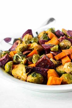 a white bowl filled with roasted vegetables on top of a table next to a spoon