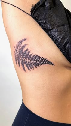 a woman's stomach with a fern leaf tattoo on her left side ribcage