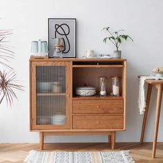 a wooden cabinet with glass doors and drawers in a living room next to a potted plant