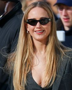 a woman wearing sunglasses and smiling for the camera while standing in front of a crowd