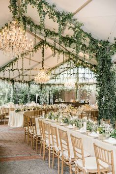 an outdoor tent with tables and chairs covered in greenery