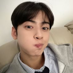 a young man wearing a suit and tie making a face while sitting on a couch