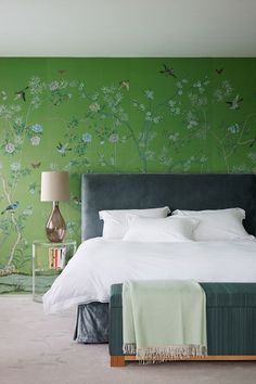 a bed sitting in a bedroom next to a green wall with flowers and birds on it