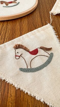 two hand embroidered pillows sitting on top of a wooden table next to each other, one with a horse