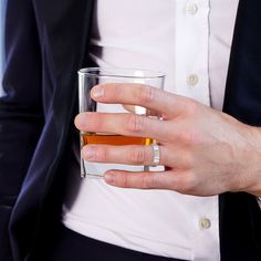 a man wearing a suit and holding a glass with something in it's hand