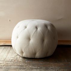 a white round foot stool sitting on top of a wooden floor next to a wall