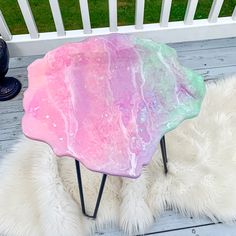 a pink and green table sitting on top of a wooden deck next to a white rug