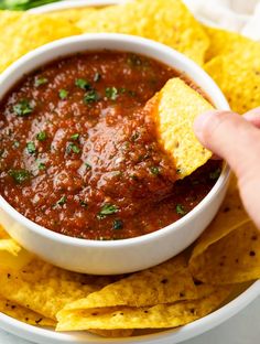 a hand dipping a tortilla chip into a bowl of salsa with tortilla chips