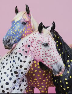 three painted horses standing next to each other on a pink background with polka dot spots