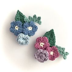 two crocheted flowers sitting next to each other on top of a white surface