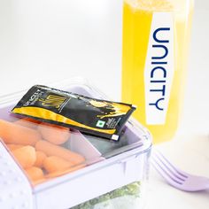 a plastic container filled with carrots next to a fork and bottle of liquid on a table