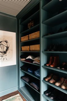 an organized closet with shoes and baskets on the shelves in front of a large painting