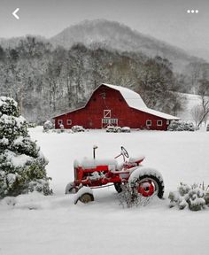 an old red tractor is parked in the snow near a barn and trees, with mountains in the background