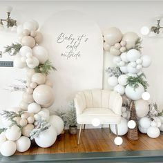 white balloons and greenery are on display in the corner of a room with a chair