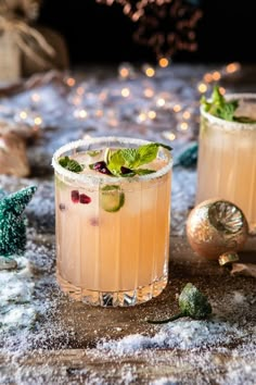 two glasses filled with drinks sitting on top of a table covered in snow and christmas decorations